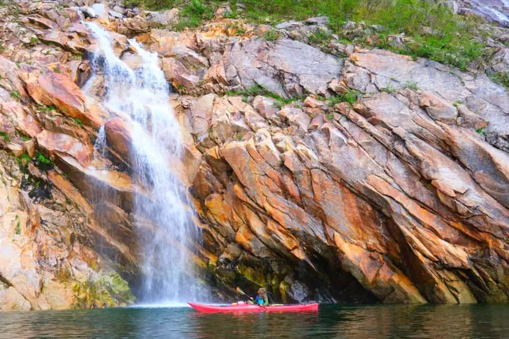 Kayaking near a waterfall in Aialik Bay on the Alaska 11-Day Grand Adventure